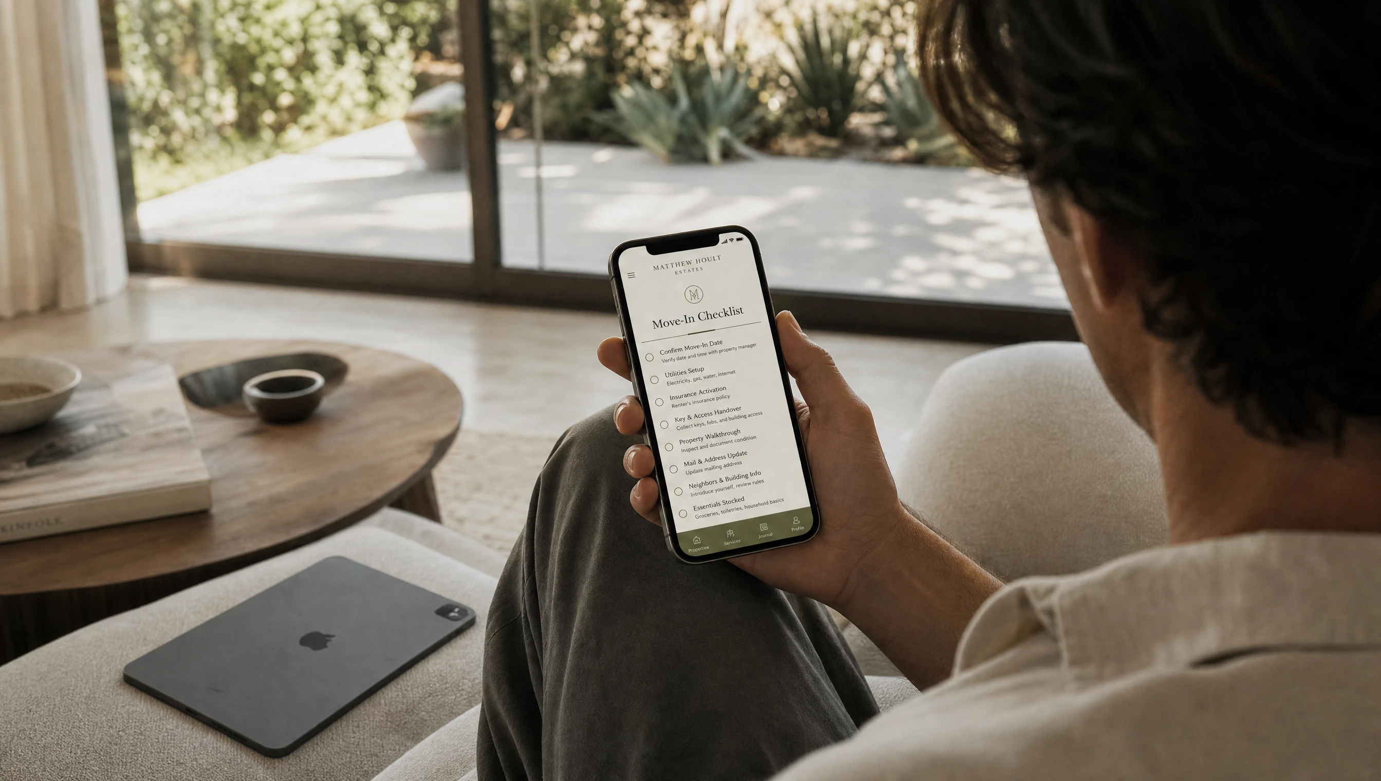 Over-the-shoulder view of a renter holding the Move-In Checklist phone mockup with an iPad nearby for the Rental Bundle